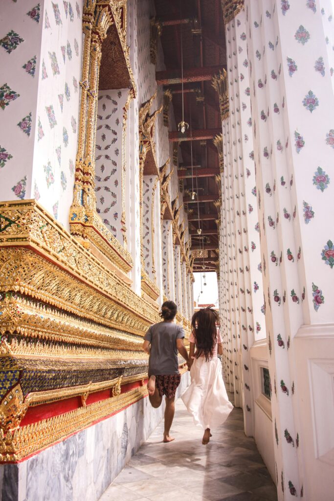 pexels-photo-4973657-4973657 A joyful couple holding hands running through a Buddhist temple corridor in Bangkok, showcasing cultural architecture.